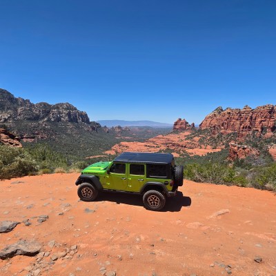 Green Jeep on a dirt road with red rock formations in the background.