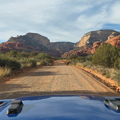 Dirt road through desert landscape with rocky cliffs and sparse vegetation.