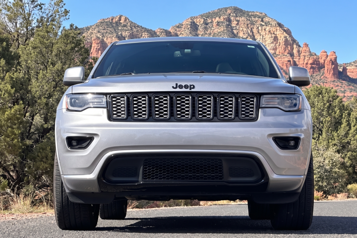 Silver Jeep SUV on road with red rock cliffs and trees in background.