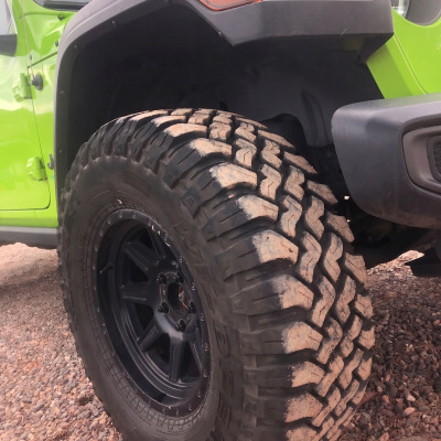 Close-up of a green off-road vehicle with large rugged tires on gravel.