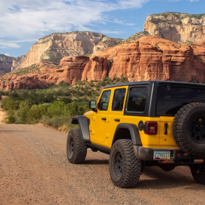 Yellow off-road vehicle on dirt road with red rock mountains in the background.