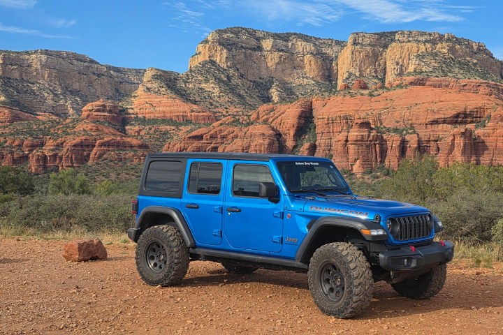 Blue SUV parked on rocky terrain with red rock cliffs in the background.