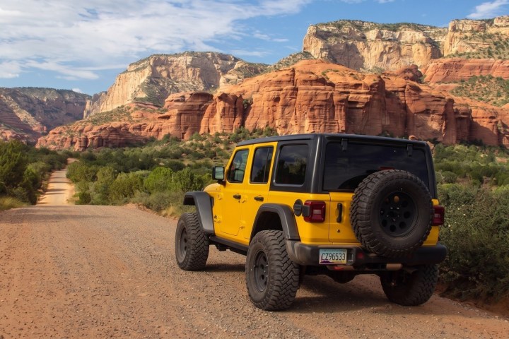 Yellow SUV on dirt road with red rock cliffs and blue sky background.