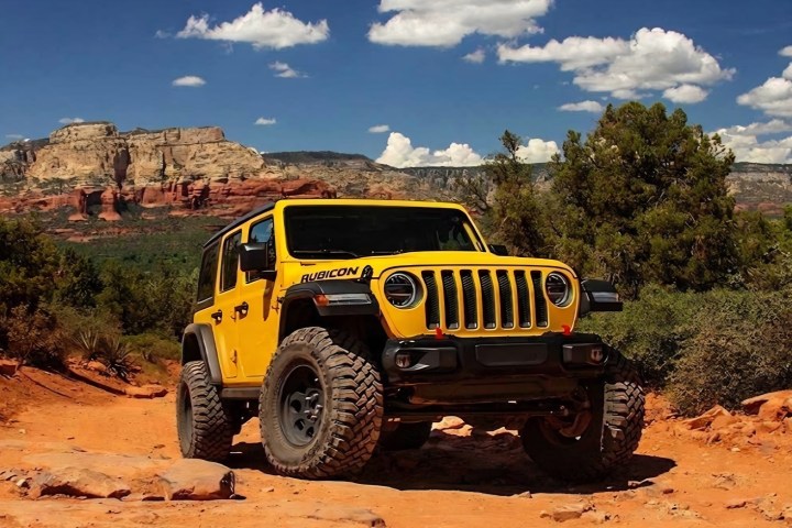 Yellow off-road vehicle on a rocky desert trail with cliffs in the background.